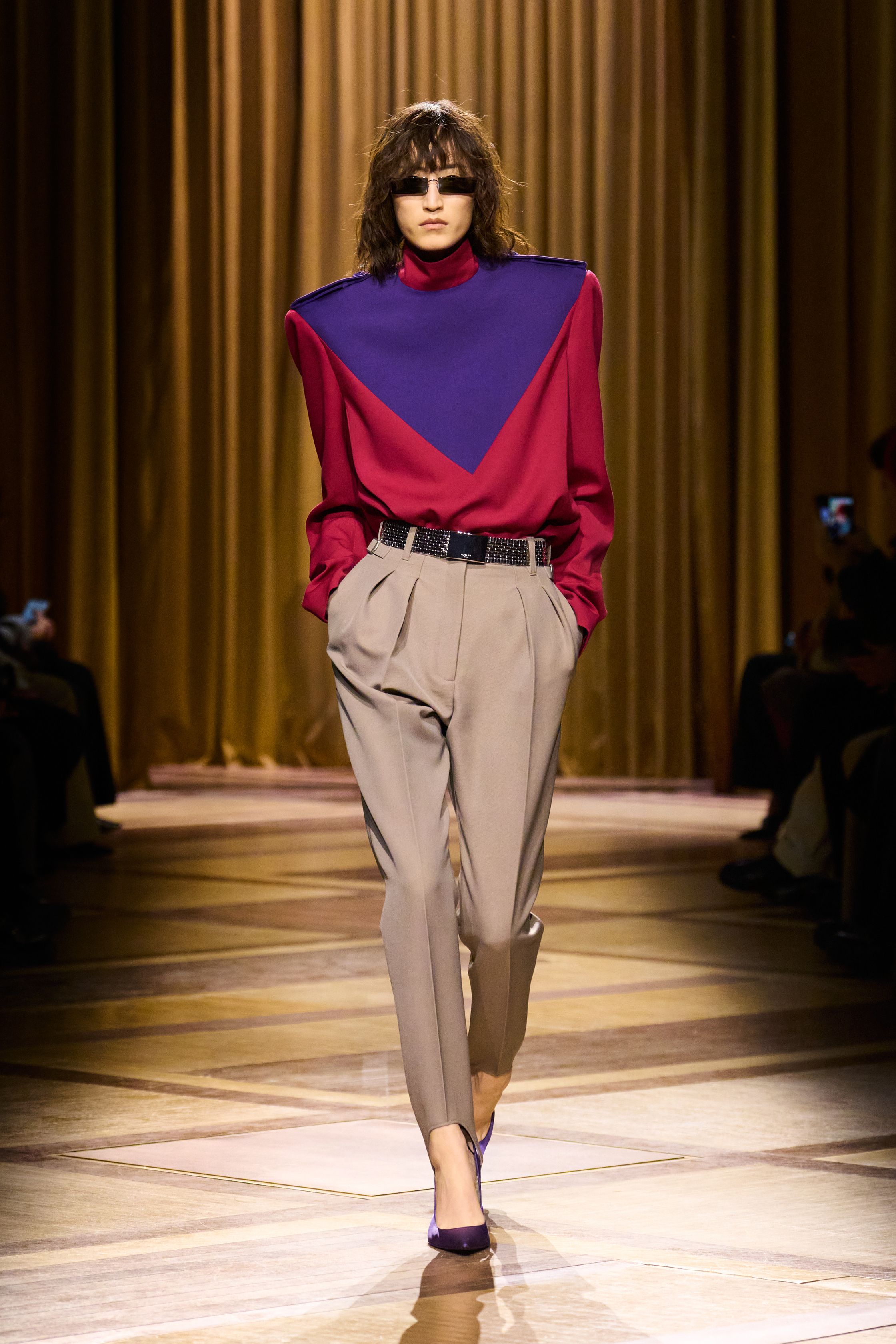 Mugler 本季继续强化品牌最核心的雕塑性感：极端肩线、收紧腰部与流畅长裤塑造出未来感女性轮廓。紫色权力套装、金属光泽衬衫和皮革裙装让整场秀既强势又华丽，仿佛科幻电影中的都市女主角-顽石频道趋势研究